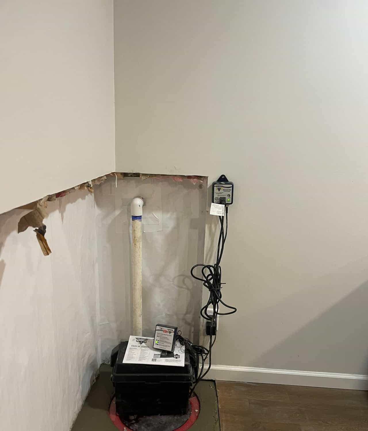 Close view of a sump pump battery backup box on a lidded sump pit with a discharge pipe and controller.