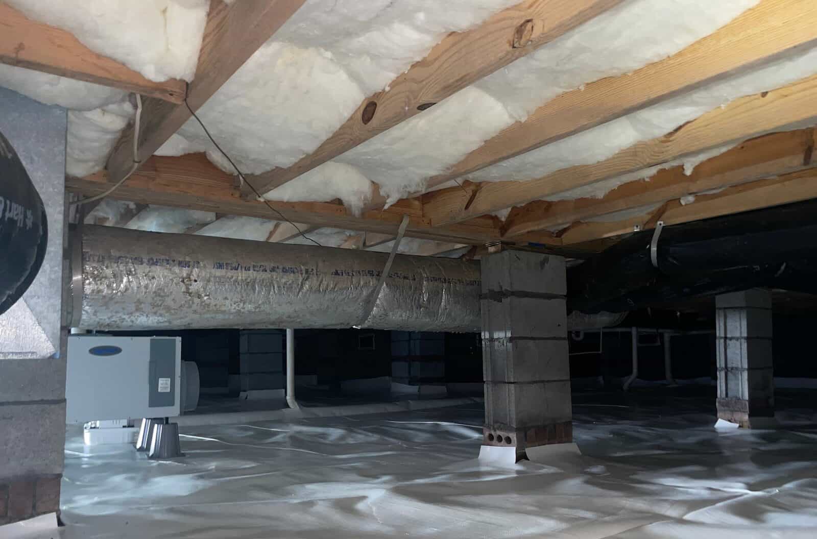 Dehumidifier set on a white lined crawl space floor near block piers and ductwork.