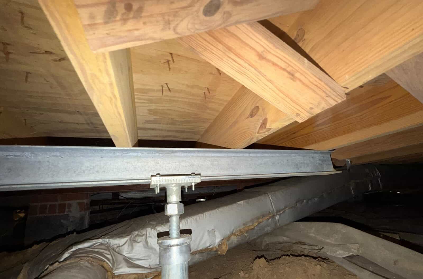 Steel beam under floor joists supported by an adjustable steel post next to insulated ductwork.