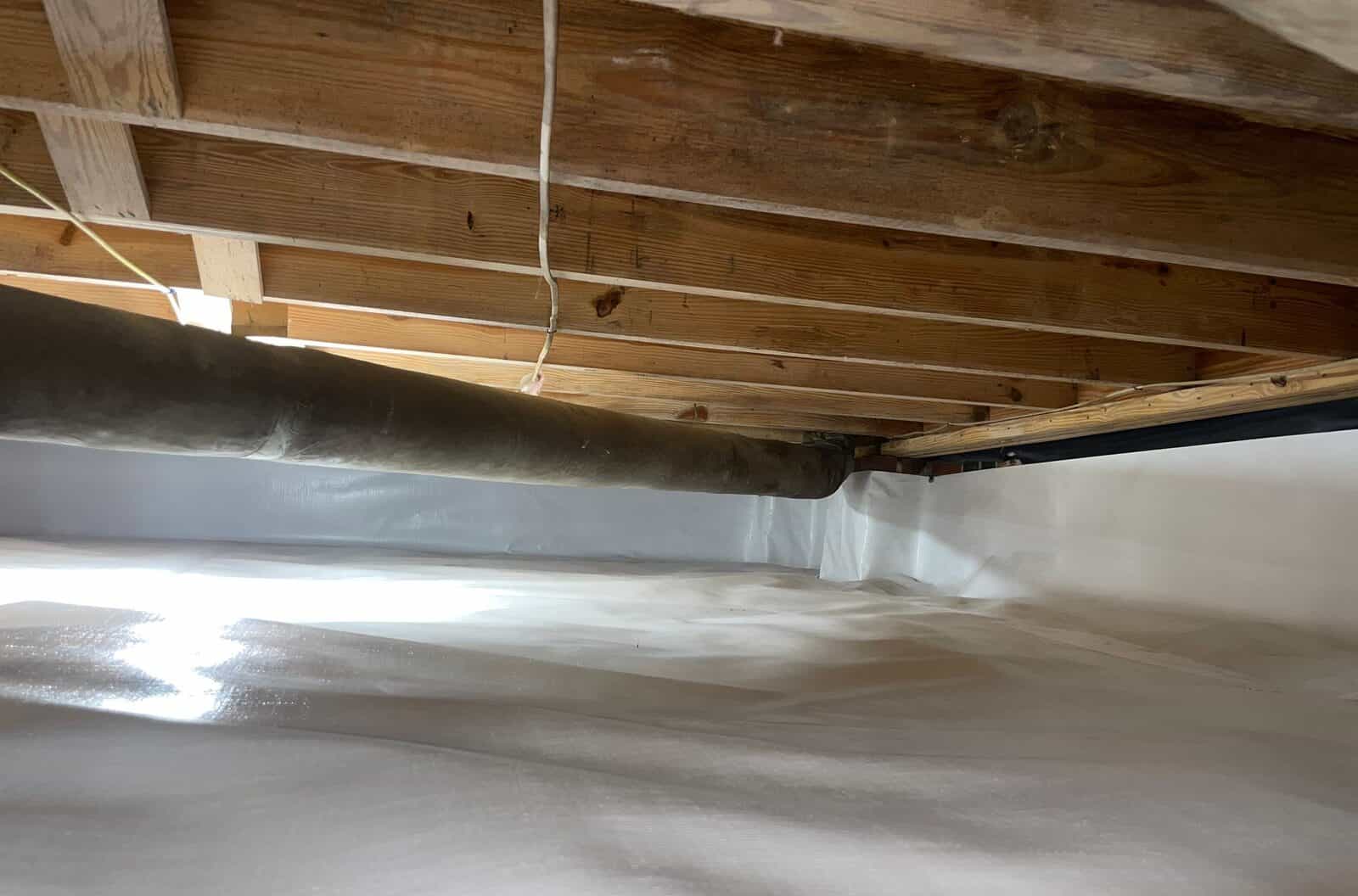 Duct running under joists above a crawl space with liner on the floor and walls.