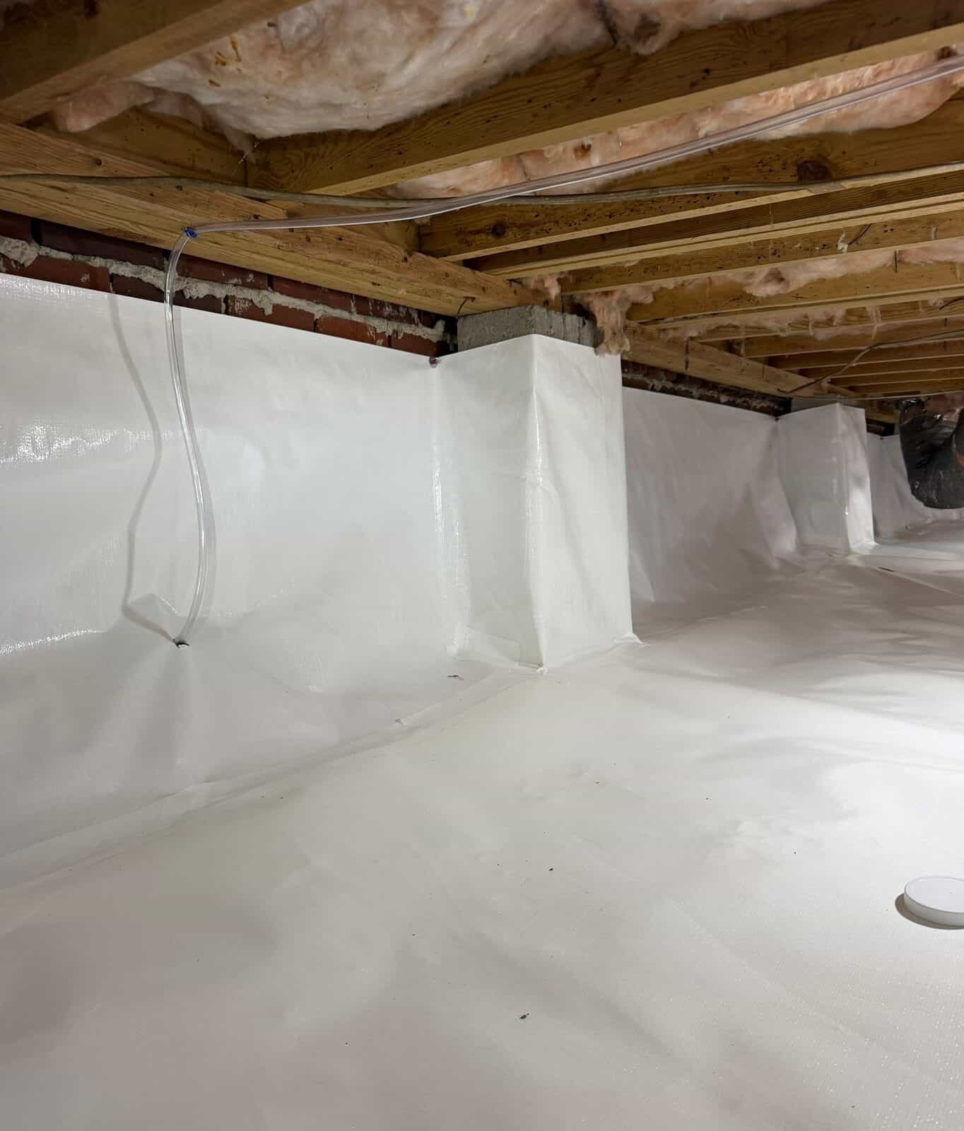 Brick crawl space walls and piers covered in white liner with a clear drain line along the wall.