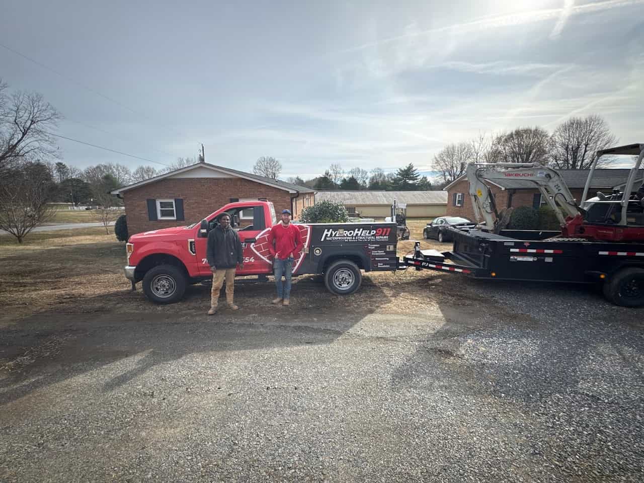 HydroHelp911 Crawl Space & Foundation Repair crew with branded truck, hauling a mini excavator on a trailer.