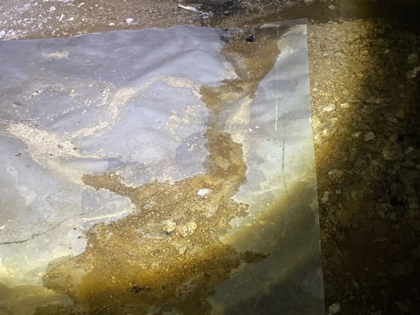 Water and mud on top of a torn plastic ground cover in a crawl space
