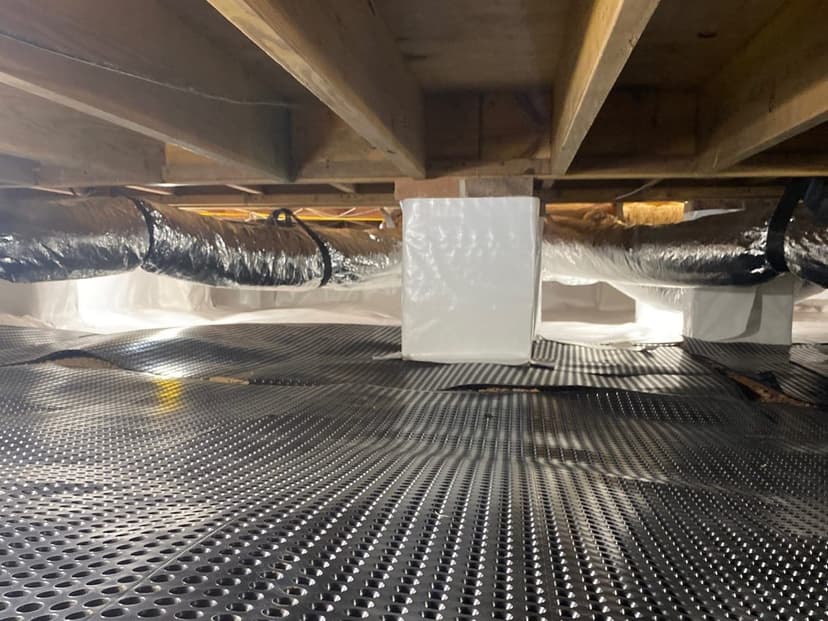 Dimpled drainage matting laid across a crawl space floor under the floor framing