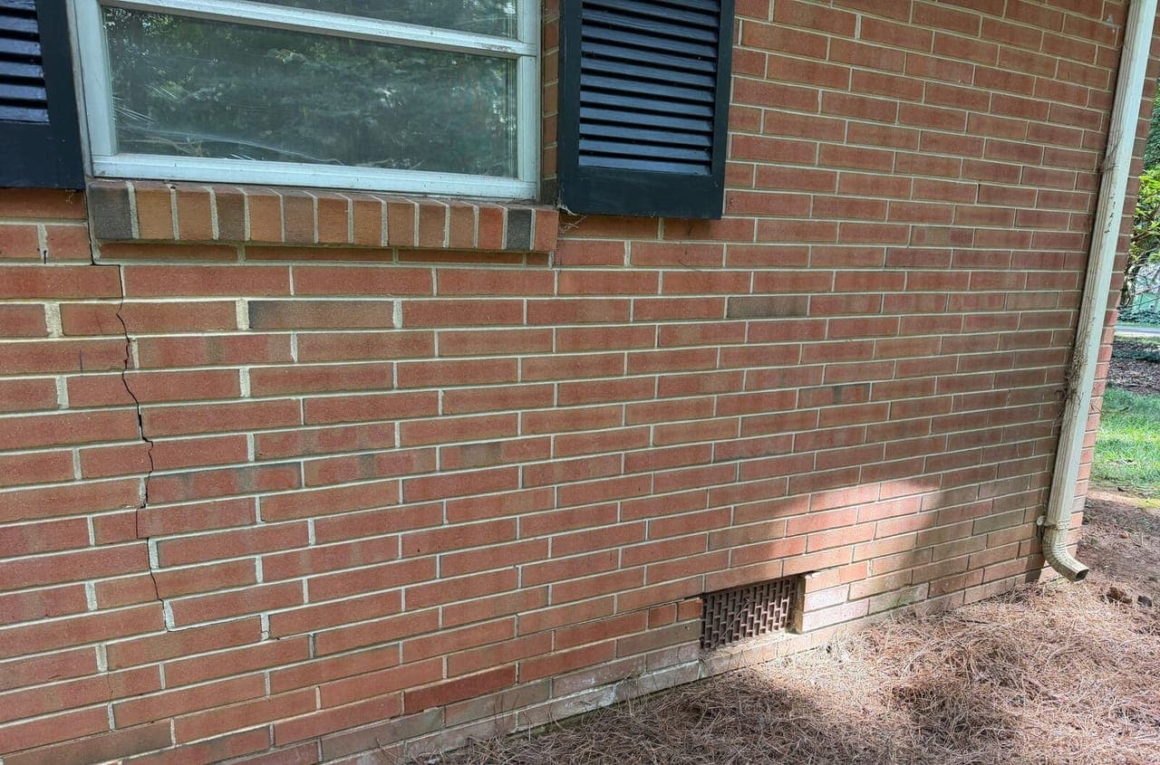 A crack running down a brick wall from the corner of a window