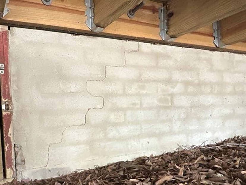 A stair step crack in a painted block foundation wall in a crawl space