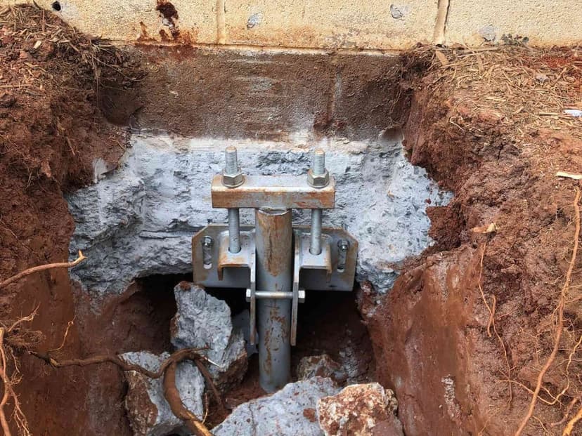 A steel push pier bracket fastened under a concrete footing in an excavation