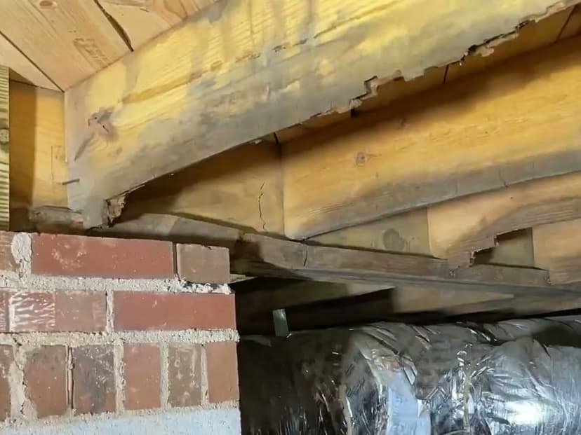 A cracked, decayed floor joist over a brick pier in a crawl space
