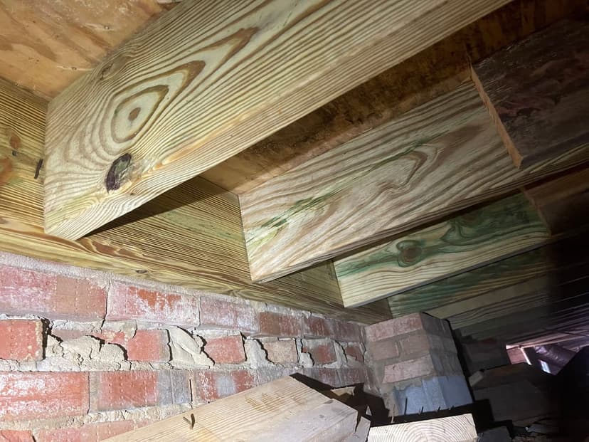 New floor joists resting on a brick foundation wall in a crawl space