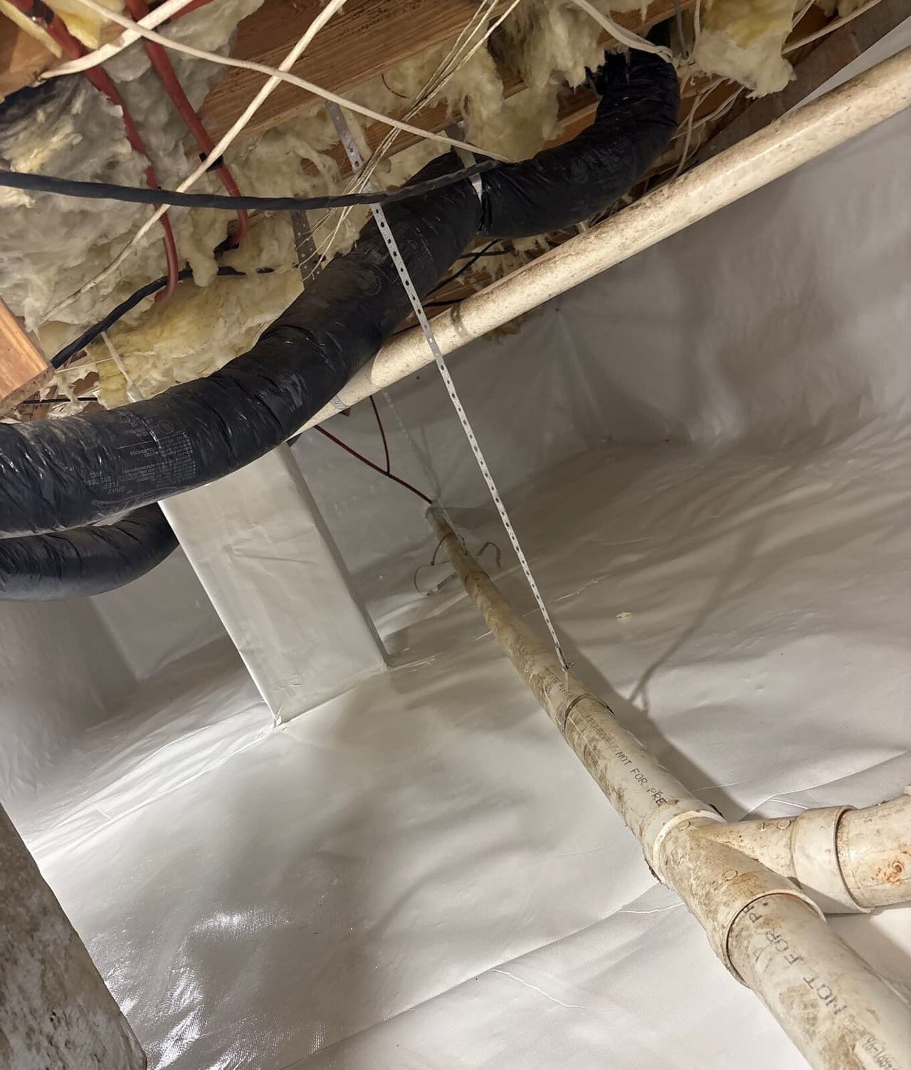 White liner covering crawl space floor, walls and a pier with pipes and ducts above.
