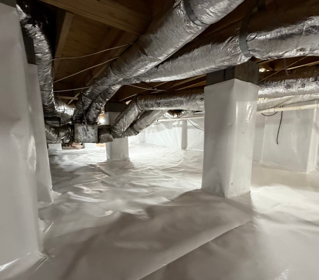 White liner covering a crawl space floor and piers beneath silver insulated ductwork.