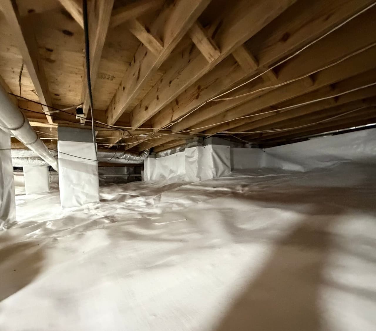 Wide crawl space view with white liner on floor and walls under exposed wood joists.
