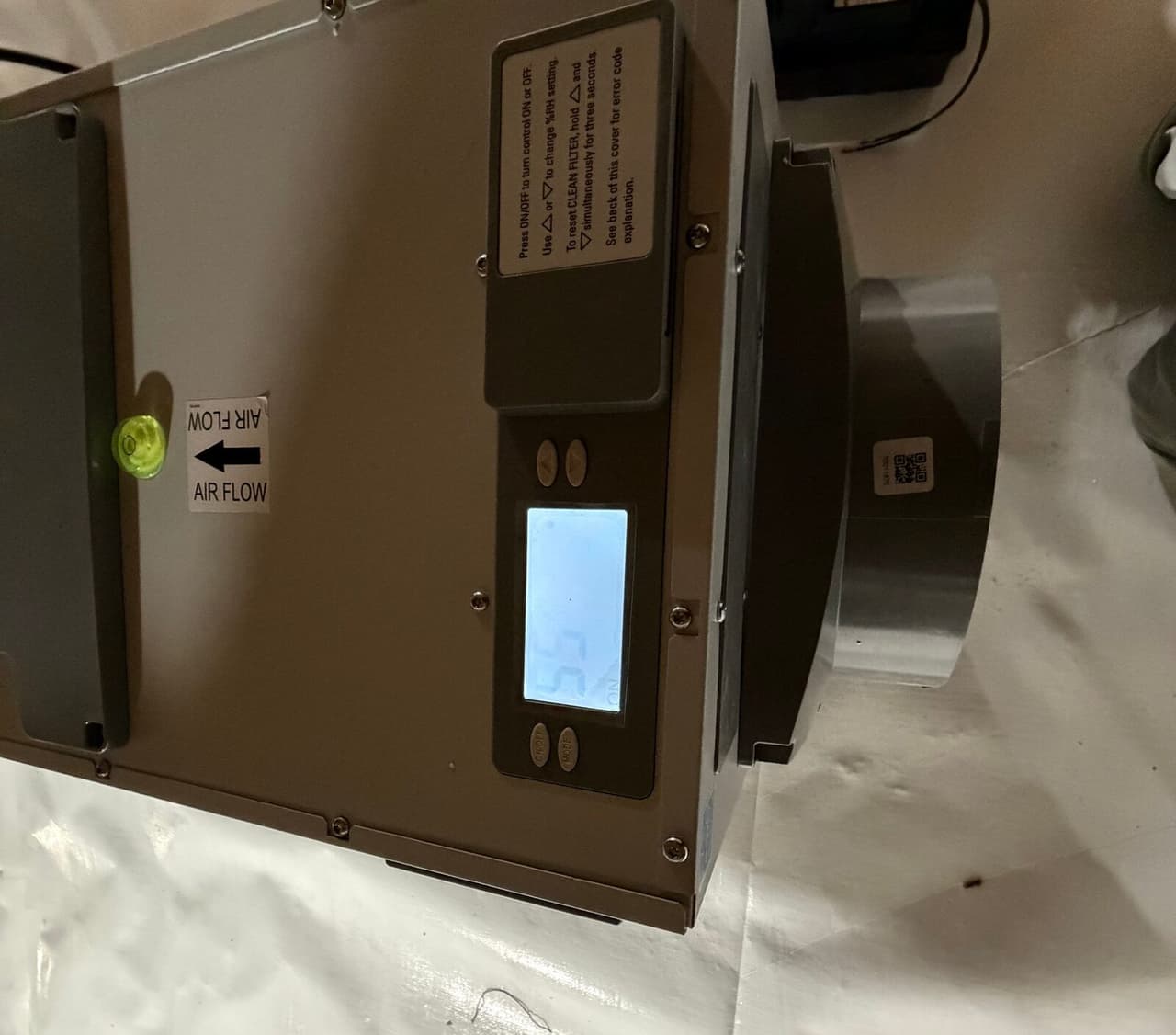 Close view of a dehumidifier with a lit display sitting on white crawl space liner.