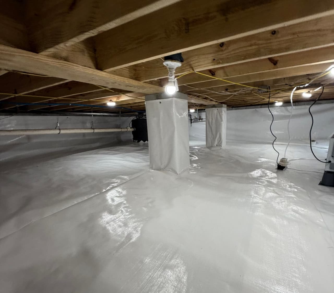 Bright crawl space with white liner on floor and walls, wrapped piers and ceiling lights.