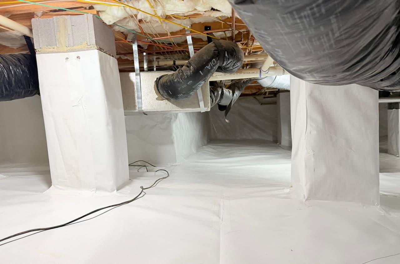 Crawl space piers wrapped in white liner with liner covering the floor beneath ducts.