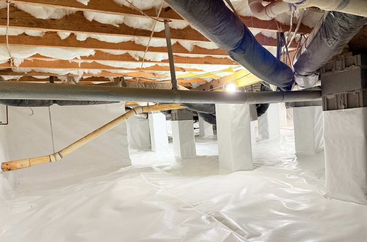 Crawl space with white liner covering the floor and wrapped piers beneath ducts and insulated joists.