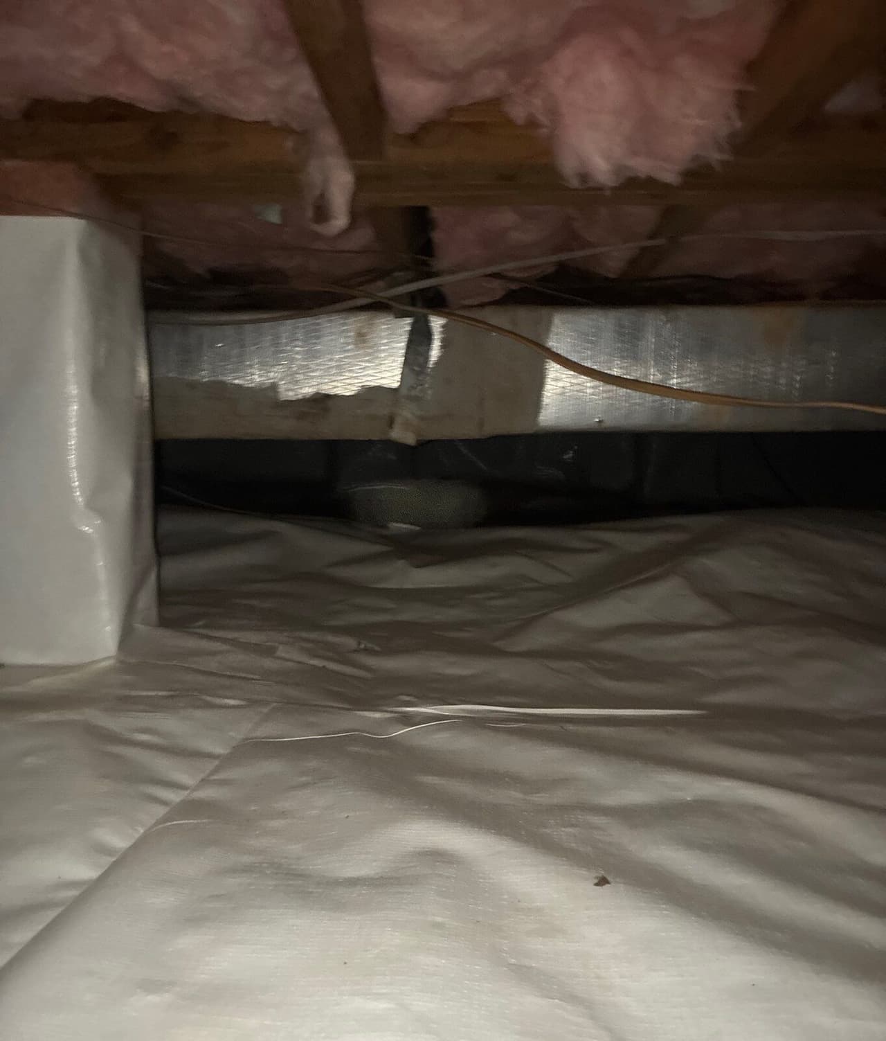 Crawl space with white liner on the floor, a taped seam and a wrapped pier.