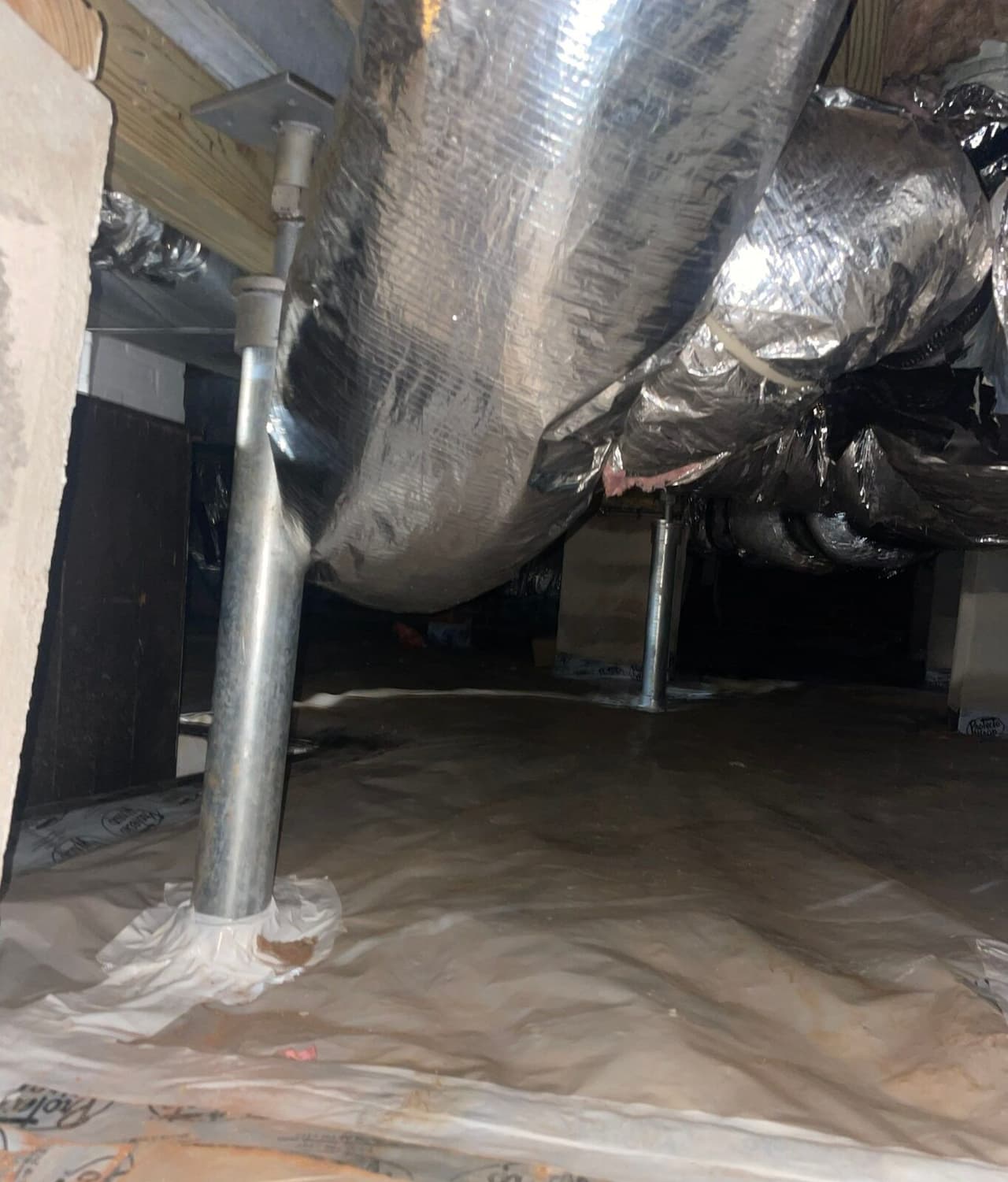 Steel support posts under a beam in a crawl space, with the vapor barrier taped around the post base.