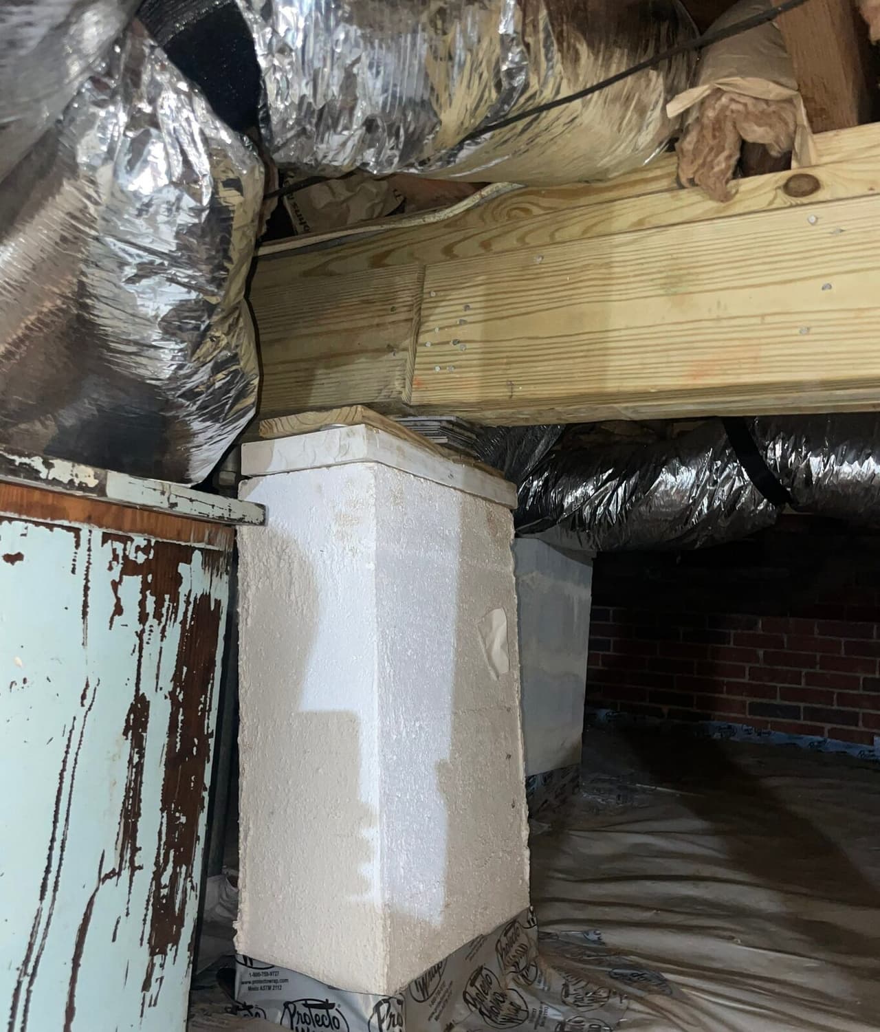 New wood beam resting on a masonry pier in a crawl space, with foil ducts and a plastic covered floor.