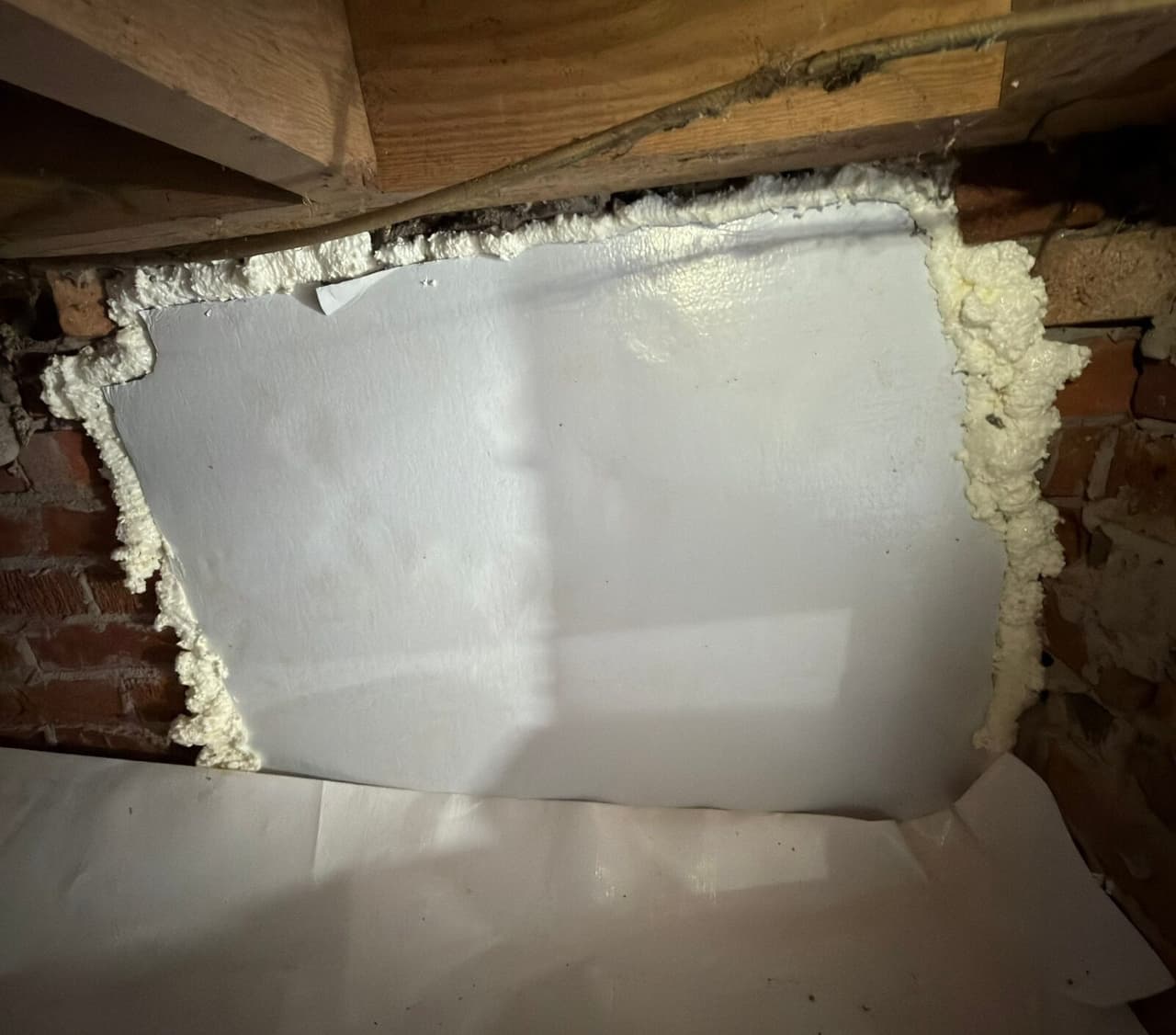Foundation vent opening covered with a white panel and sealed around the edges.