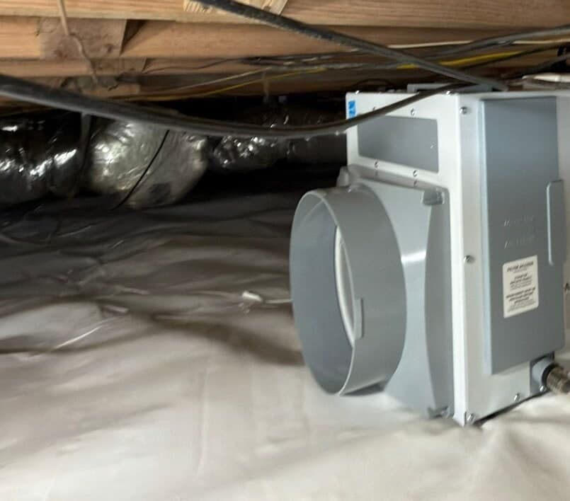 Crawl space dehumidifier sitting on a white liner beside insulated ducts under the floor joists.