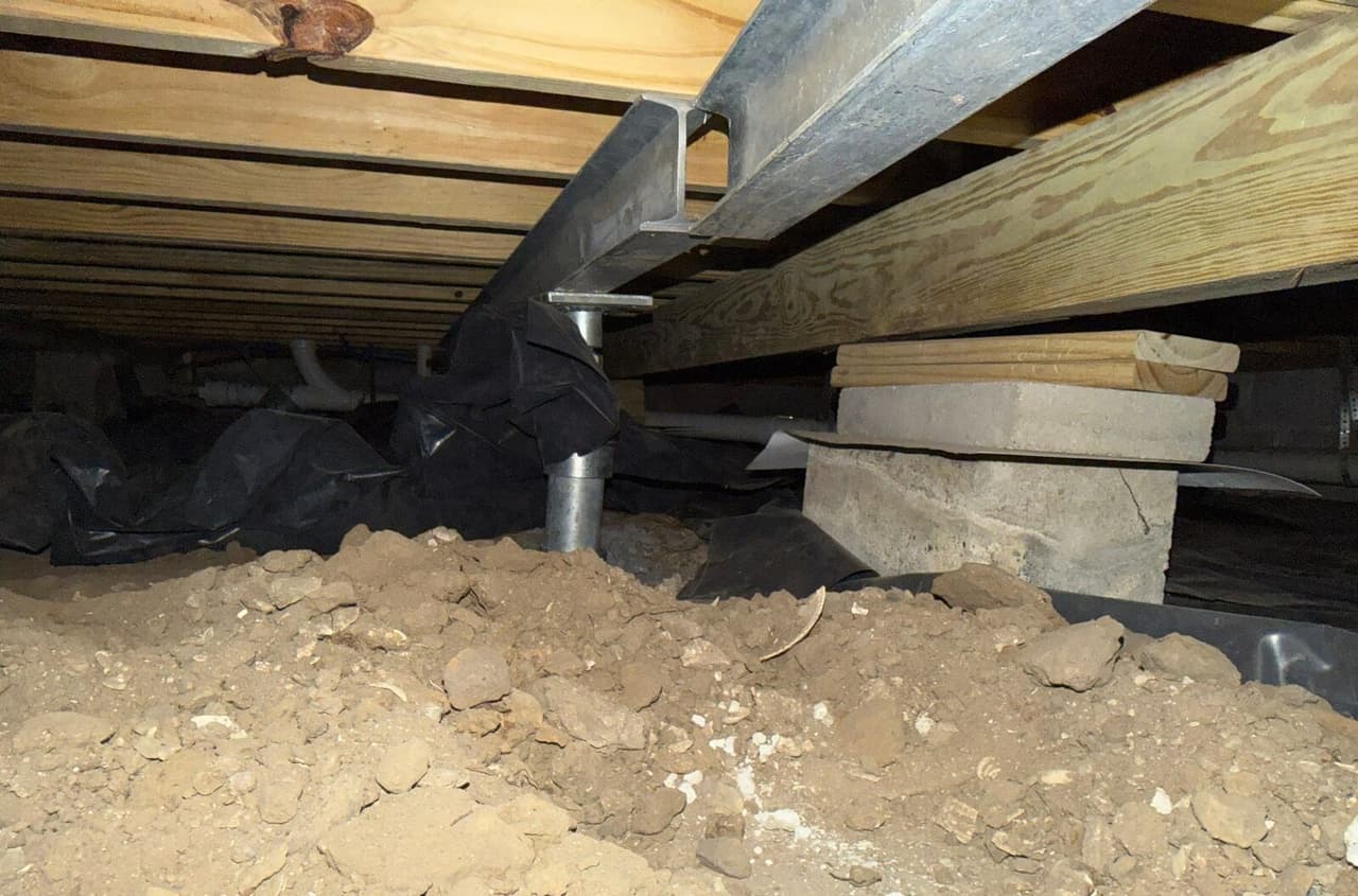 Steel beam supported by a steel post beside a block pier with wood shims under the floor framing.