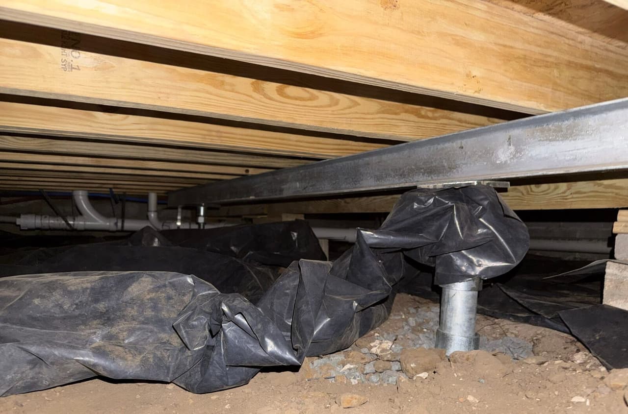 Steel beam under floor joists resting on a steel post with plastic vapor barrier bunched around it.