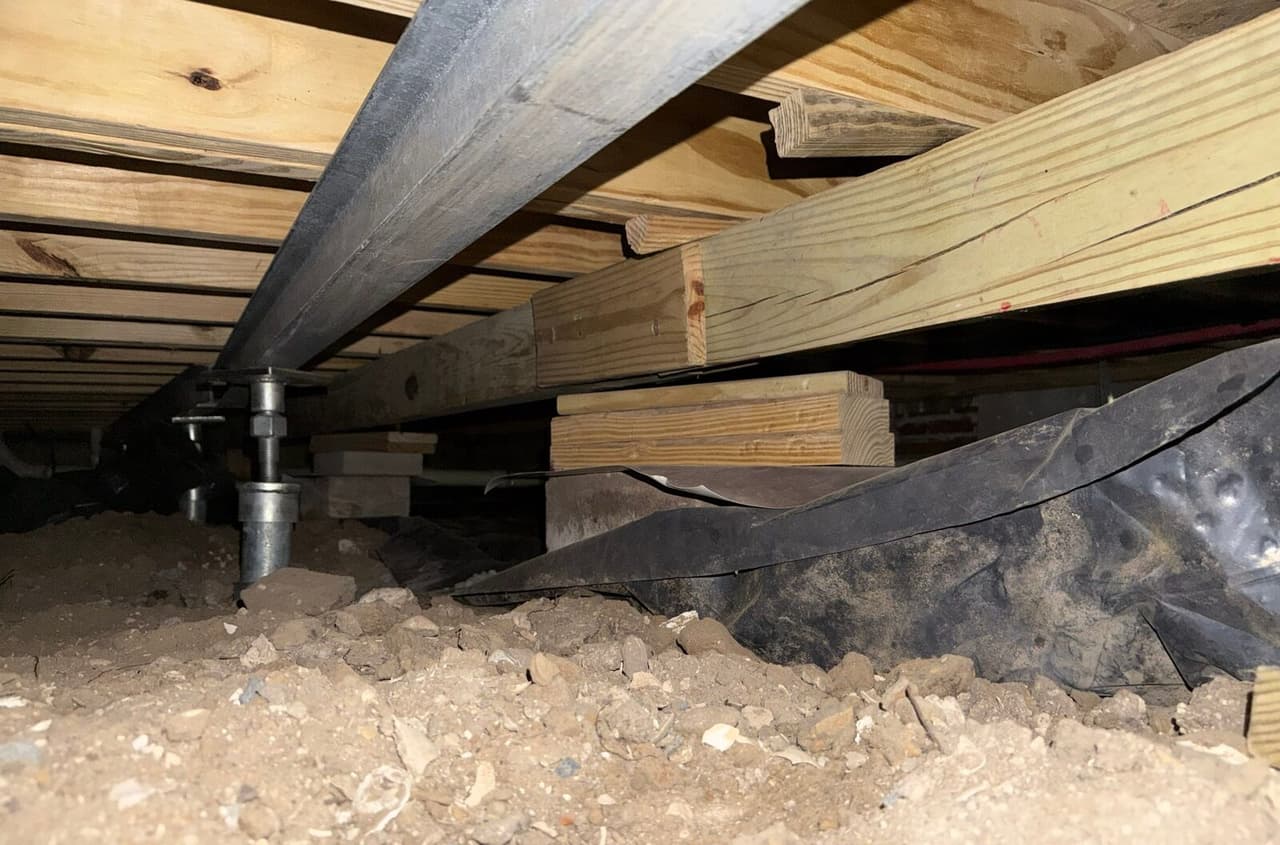Steel beam and adjustable posts installed under floor joists next to a wood girder on block piers.