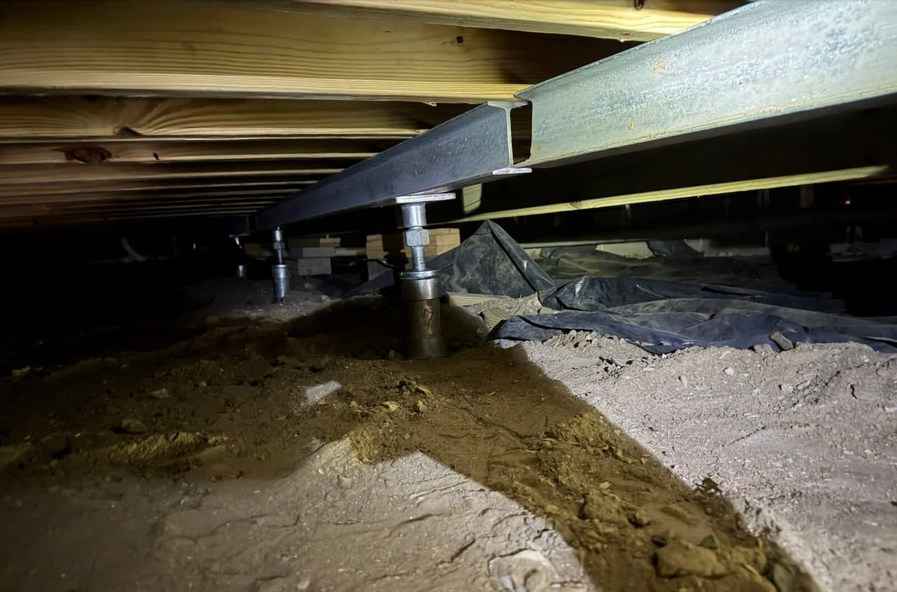 Steel beam running under floor joists supported by adjustable steel posts set in the crawl space soil.
