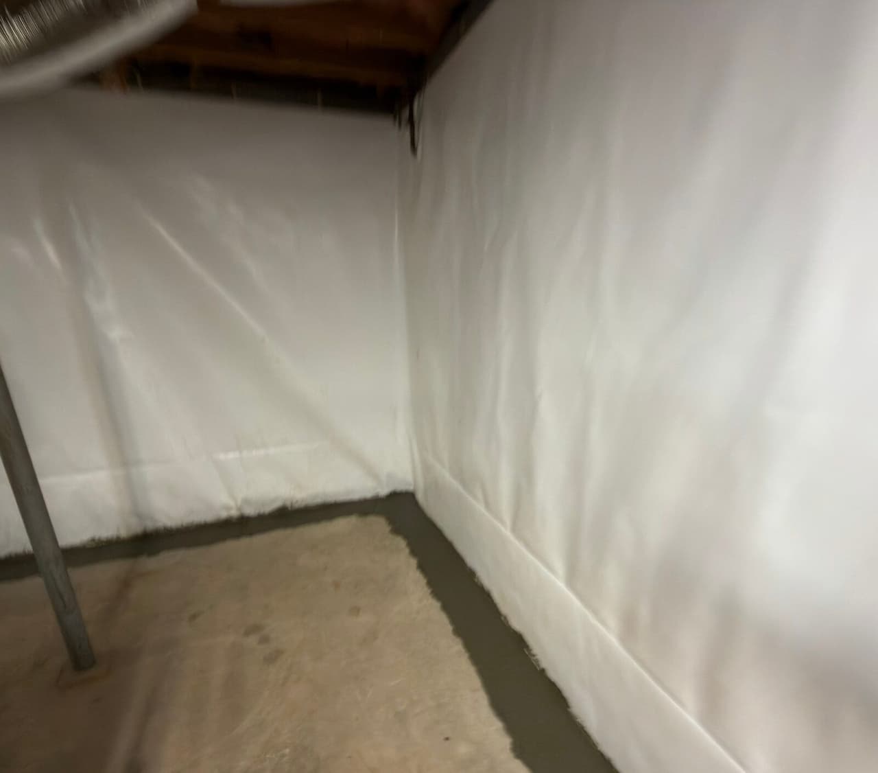 Basement corner with white liner on both walls and a fresh concrete strip along the floor edge.