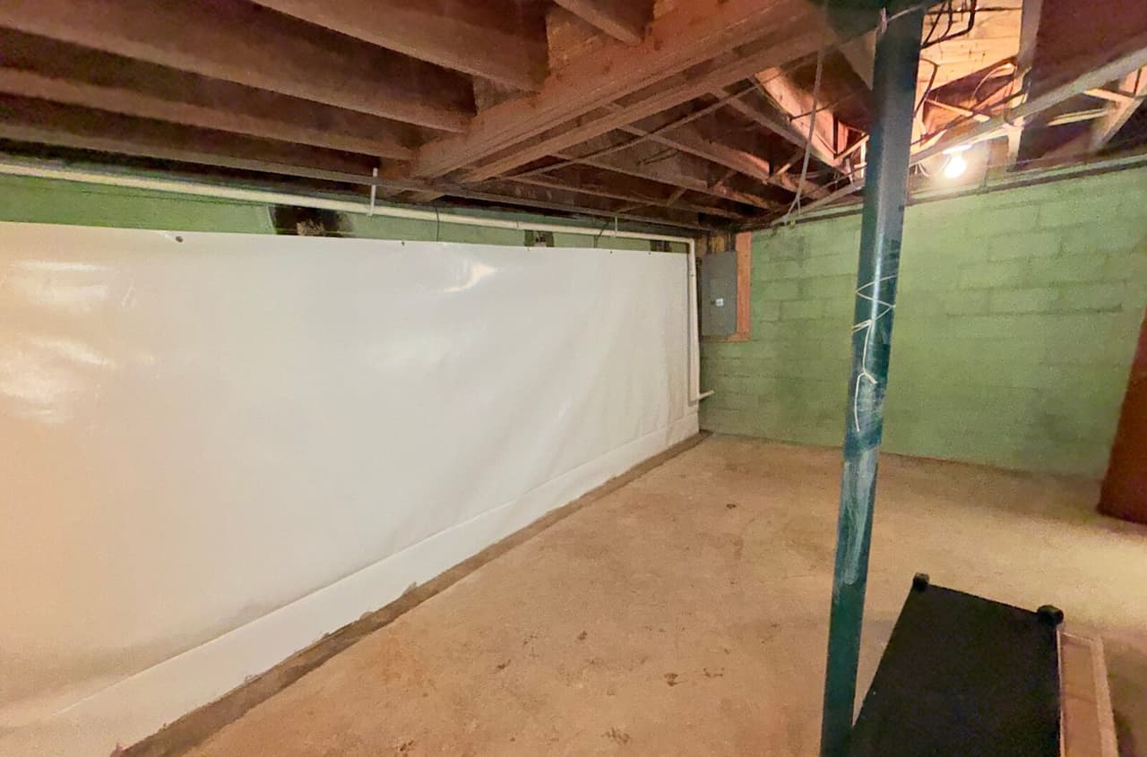 Unfinished basement with white waterproofing liner on one block wall and a patched concrete strip along the floor edge.