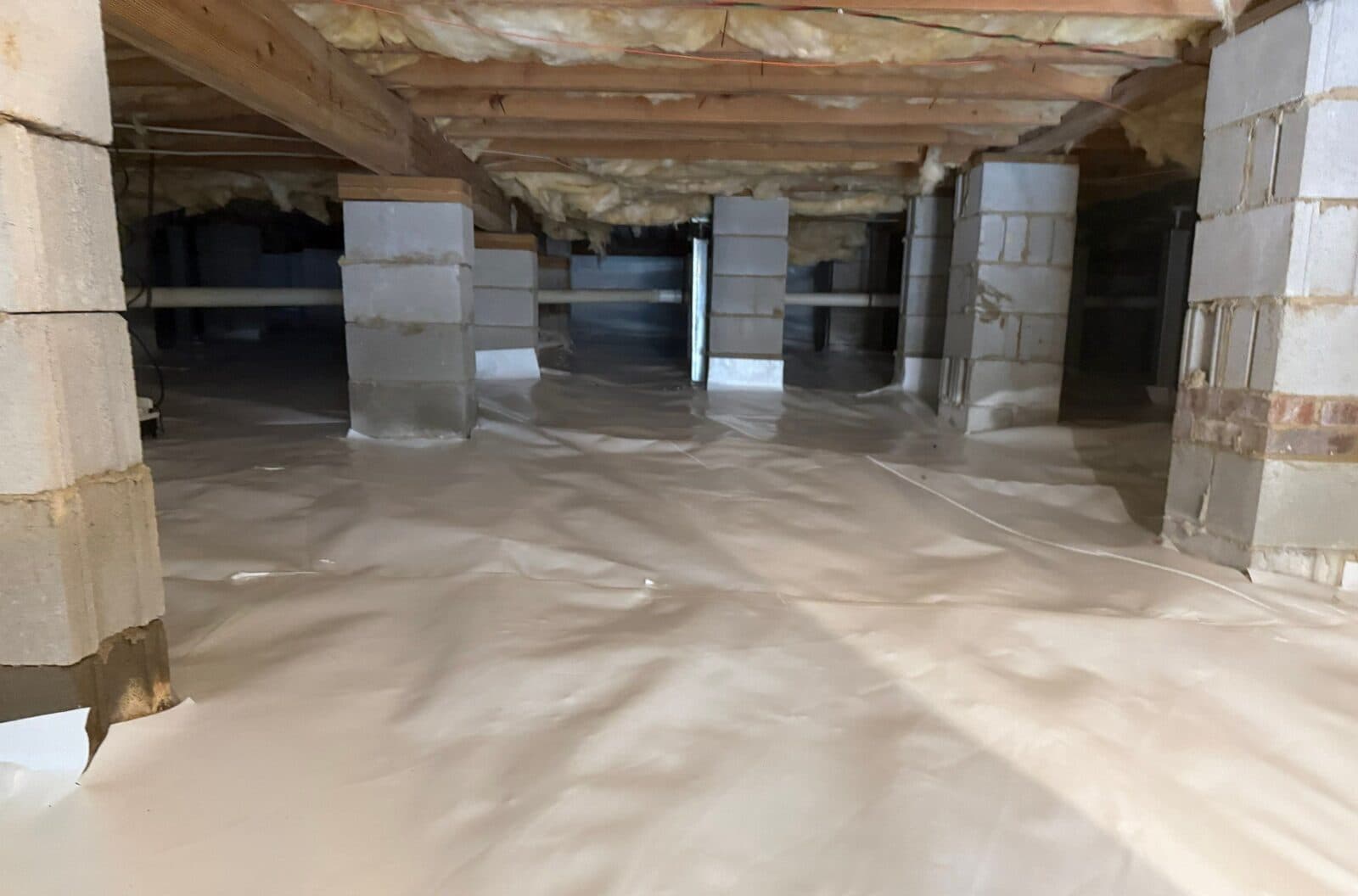 Wide view of a crawl space floor covered in white liner with rows of block piers.