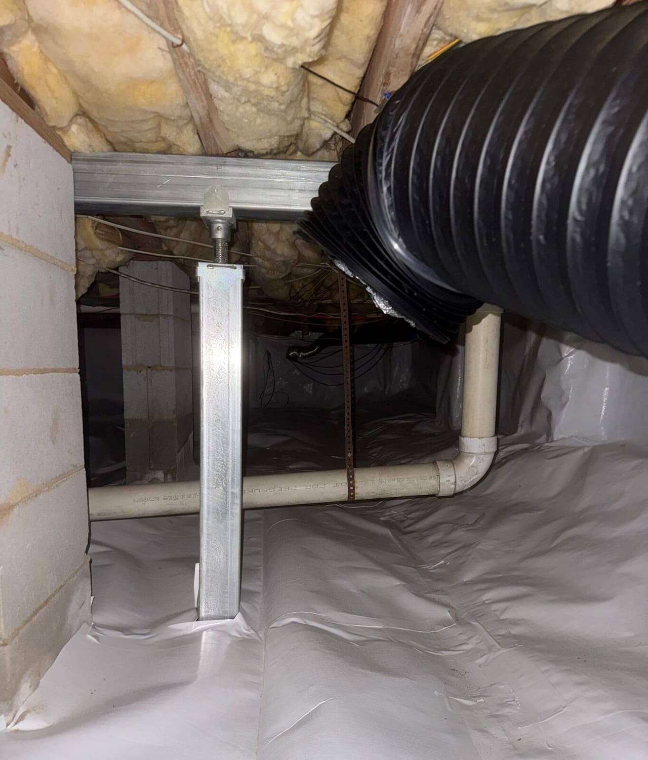 Steel support post under a metal beam in a crawl space with a white liner on the floor and walls.