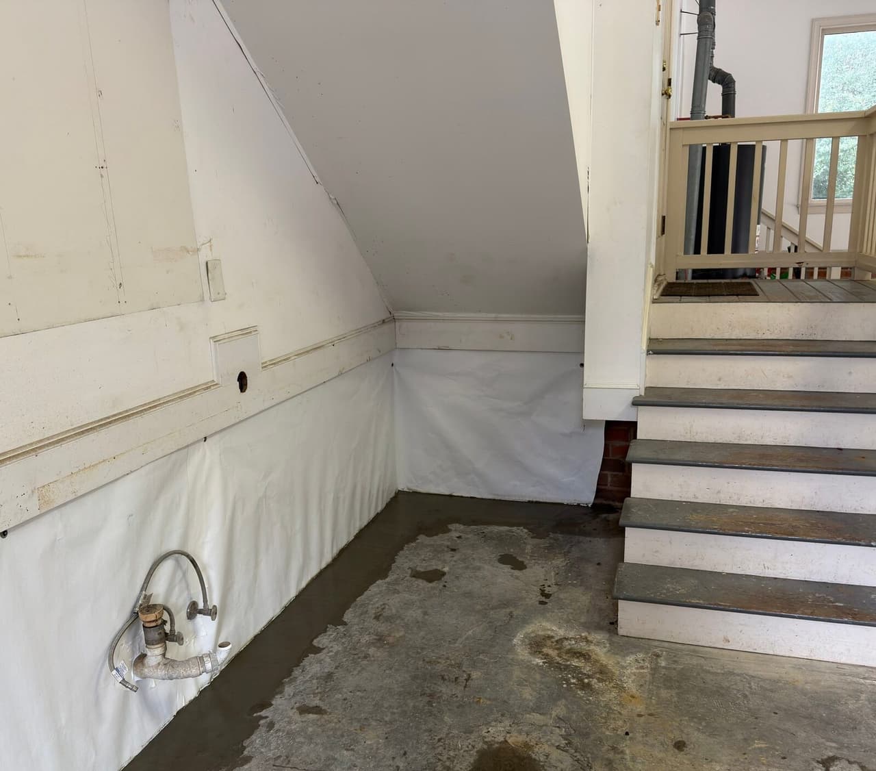 White liner along the lower walls under a staircase with fresh concrete patched along the floor edge.