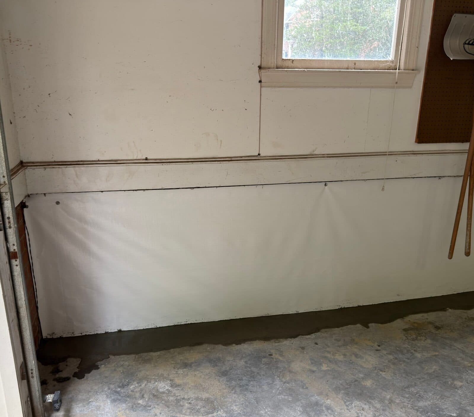 White liner fastened along the lower wall below a window with fresh concrete along the floor edge.