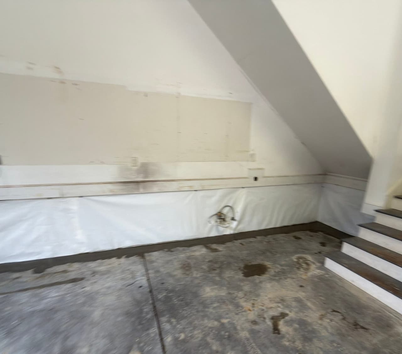Blurry view of white liner on lower walls with patched concrete at the floor edge beside stairs.