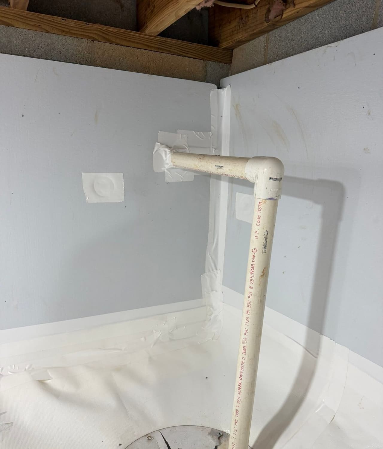 Corner of a crawl space with foam board walls, taped liner seams and a white PVC drain pipe through the wall.