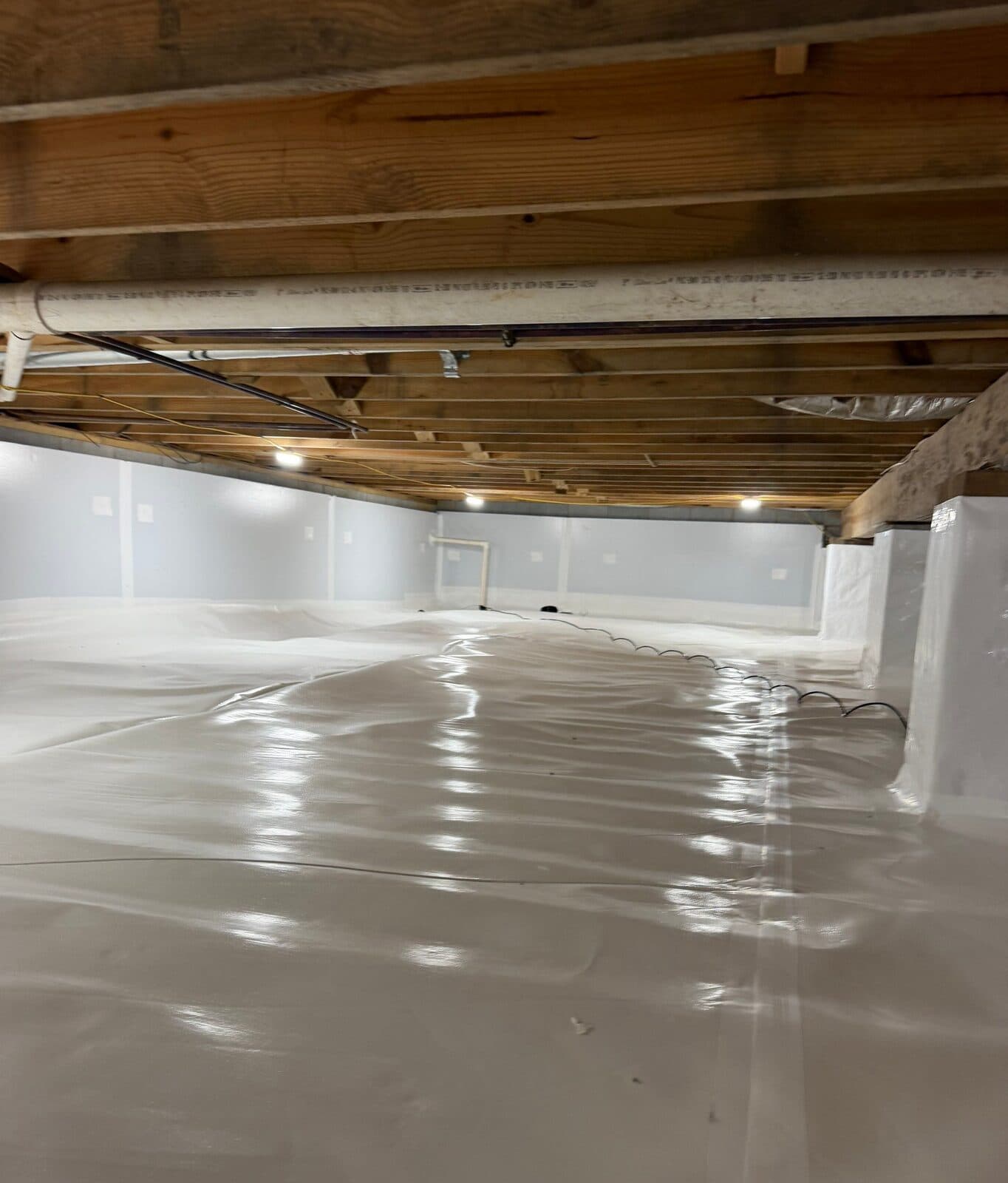 Crawl space with white liner across the floor, wrapped piers and foam board walls in the distance.