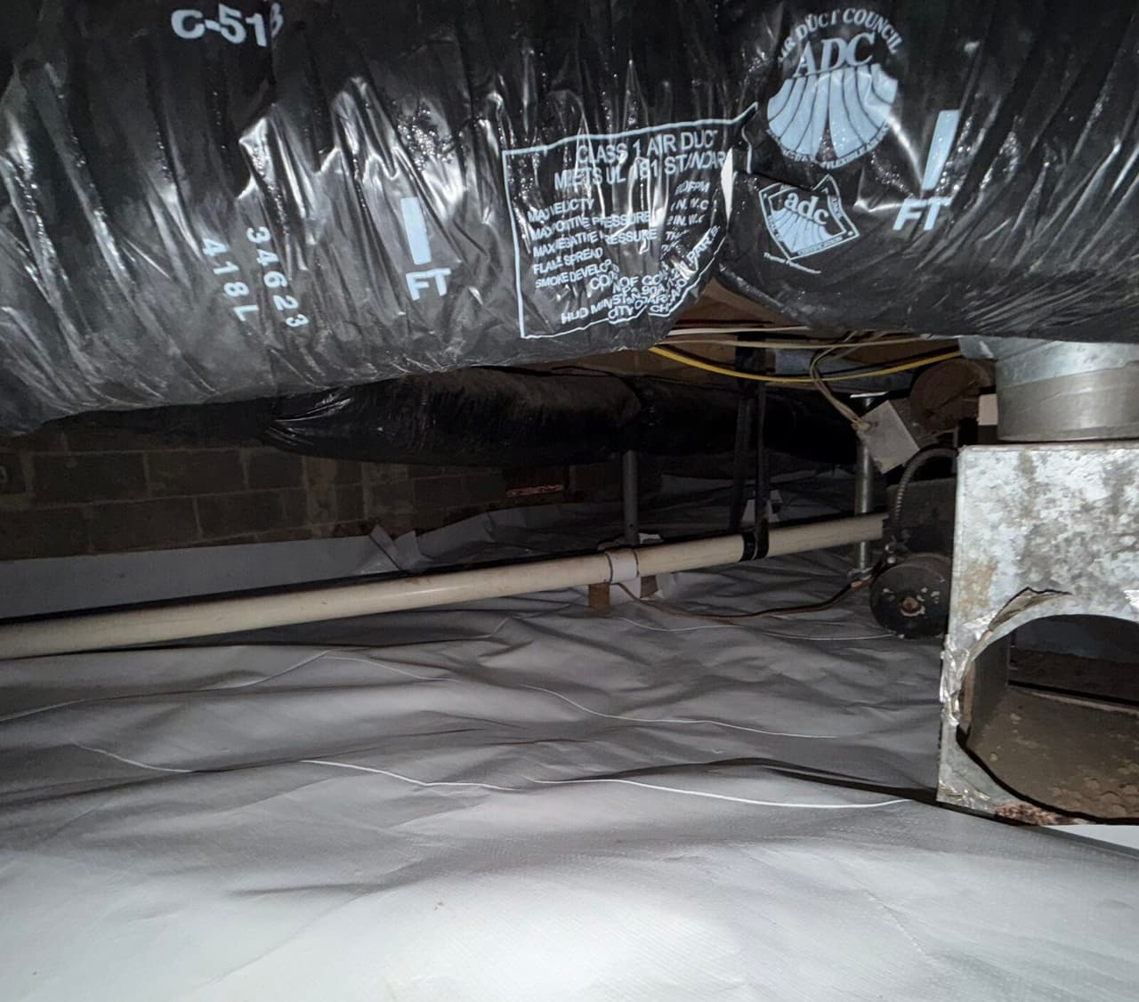 White liner covering a crawl space floor beneath insulated ductwork and a metal duct box.