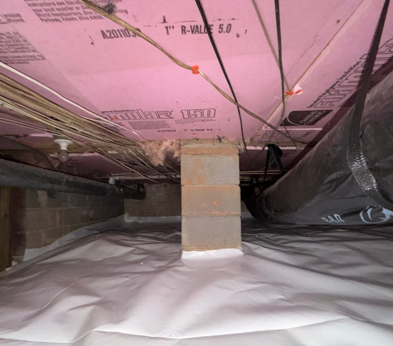 Block pier wrapped at its base by white crawl space liner under pink foam insulation and ductwork.