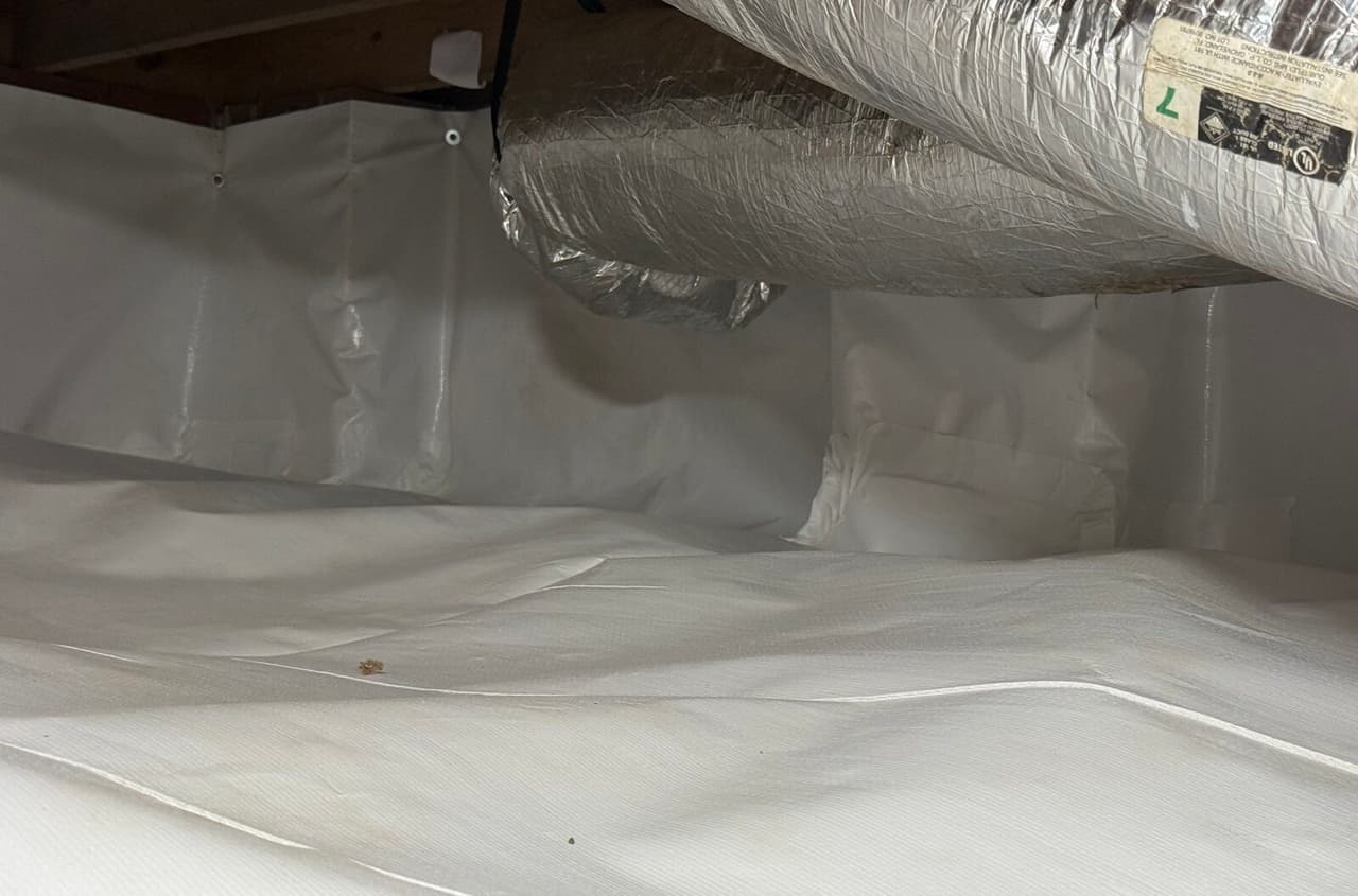 White liner covering walls and floor of a crawl space beneath insulated ductwork.