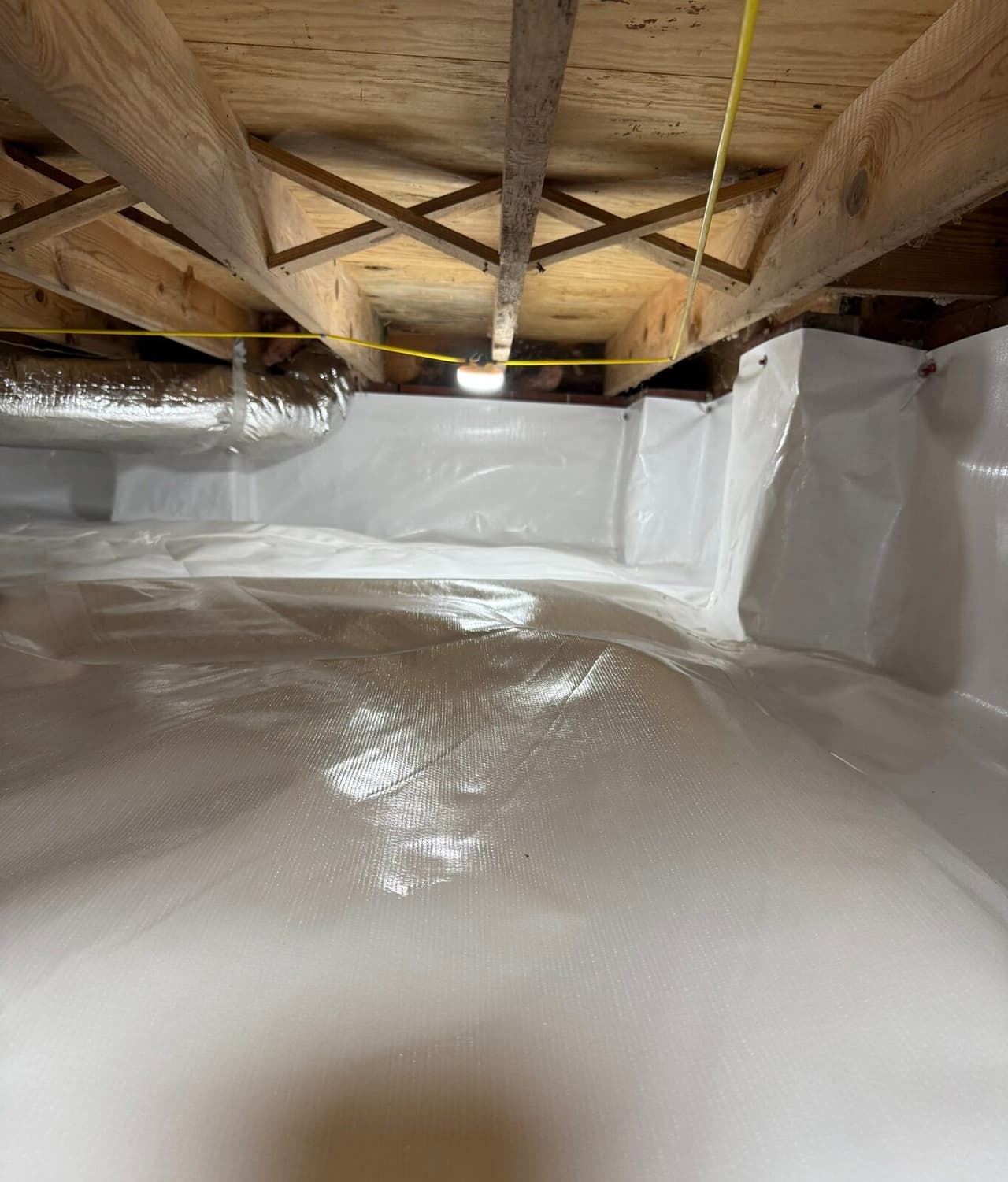 Crawl space fully lined in white liner on the floor and walls under wooden joists.