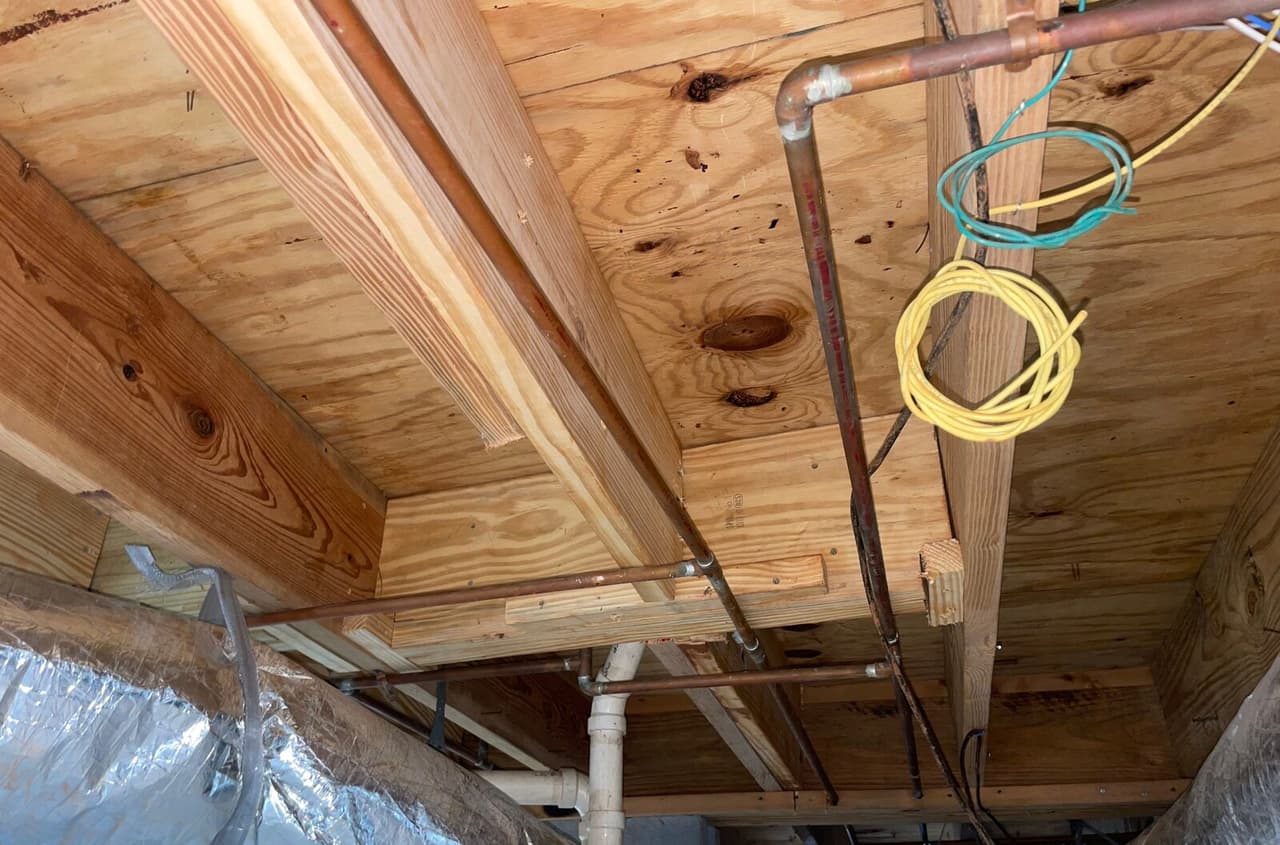 New wood joists and blocking under the subfloor with copper pipes and coiled wires nearby.