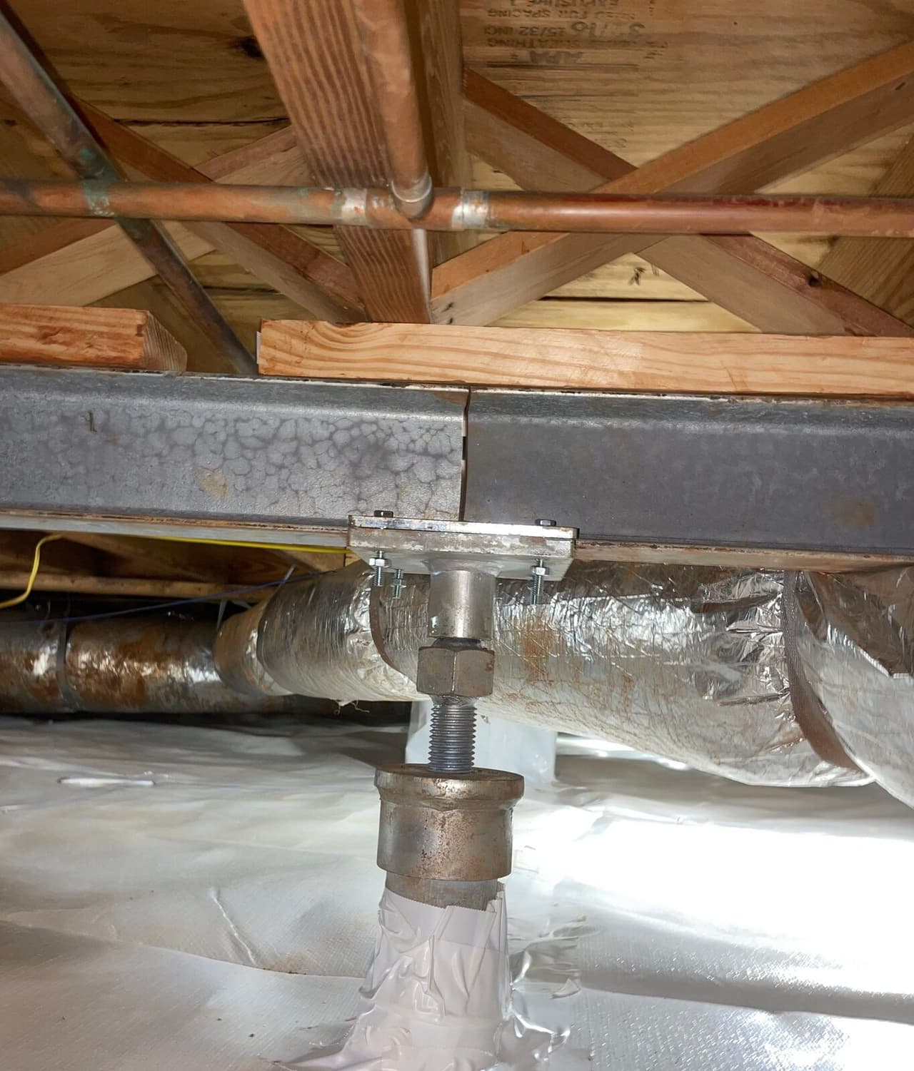 Steel support jack bolted beneath a steel beam with its base wrapped in white liner.