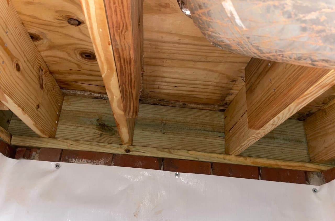 New treated rim board between floor joists above a brick wall covered with white liner.