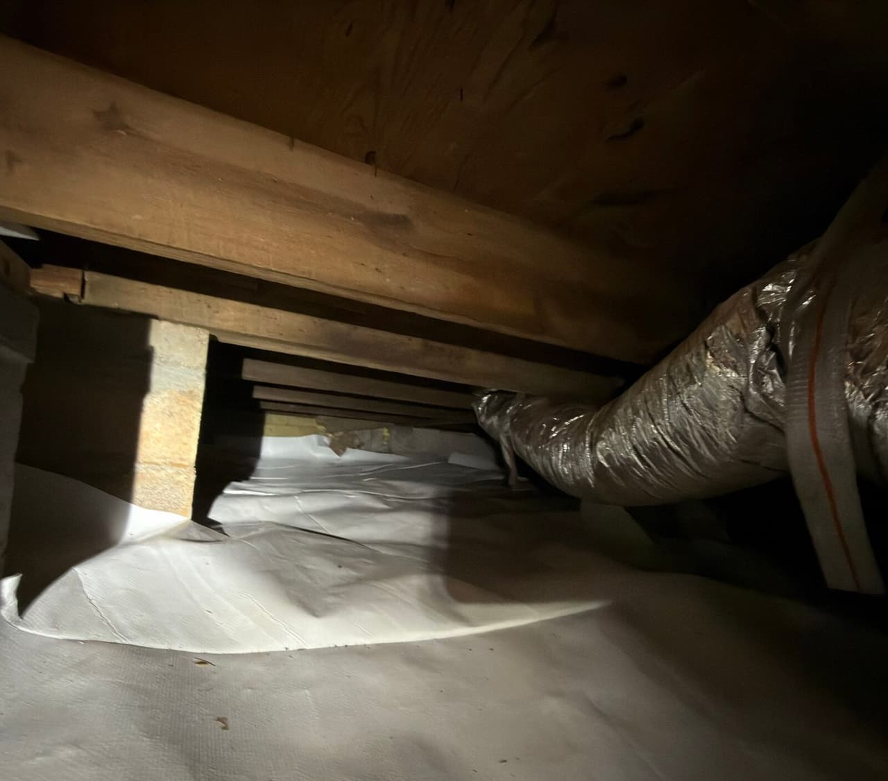 White liner covering a crawl space floor beneath wooden beams and insulated ductwork.