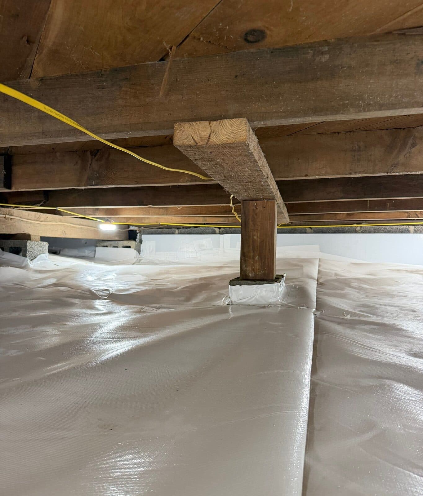 A wooden support post with its base wrapped in white liner in a fully lined crawl space.