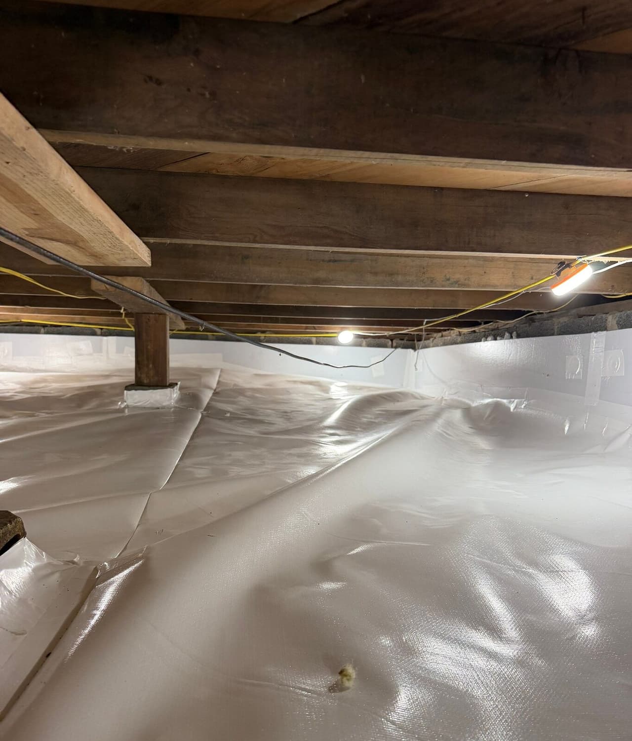 A crawl space with white liner on the floor and walls and a wrapped wooden post base.