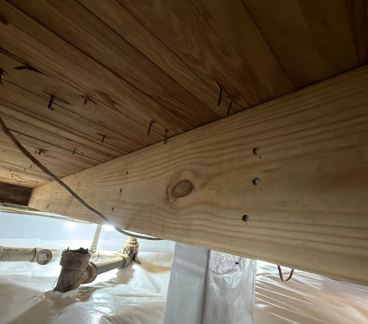 New lumber joist nailed under the subfloor with a wrapped pier and lined floor below.