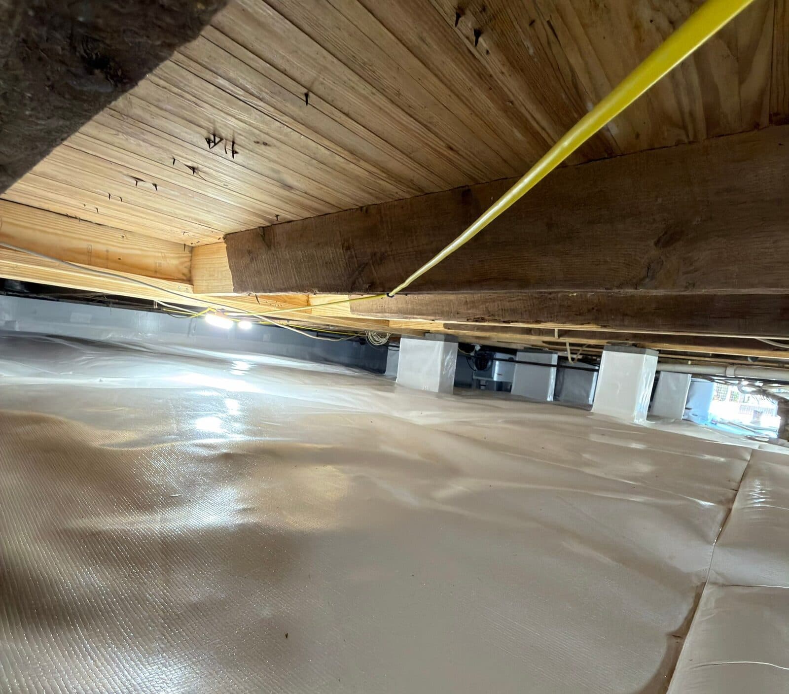 Wide view of a crawl space with liner covering the floor and wrapped support piers.